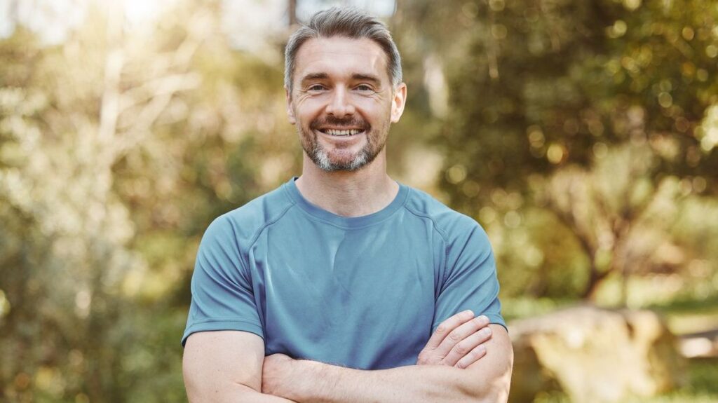 Senior, fitness and portrait of man with arms crossed in a park happy with workout, running or results. Exercise, face and elderly male runner smile in forest for training, workout or body challenge